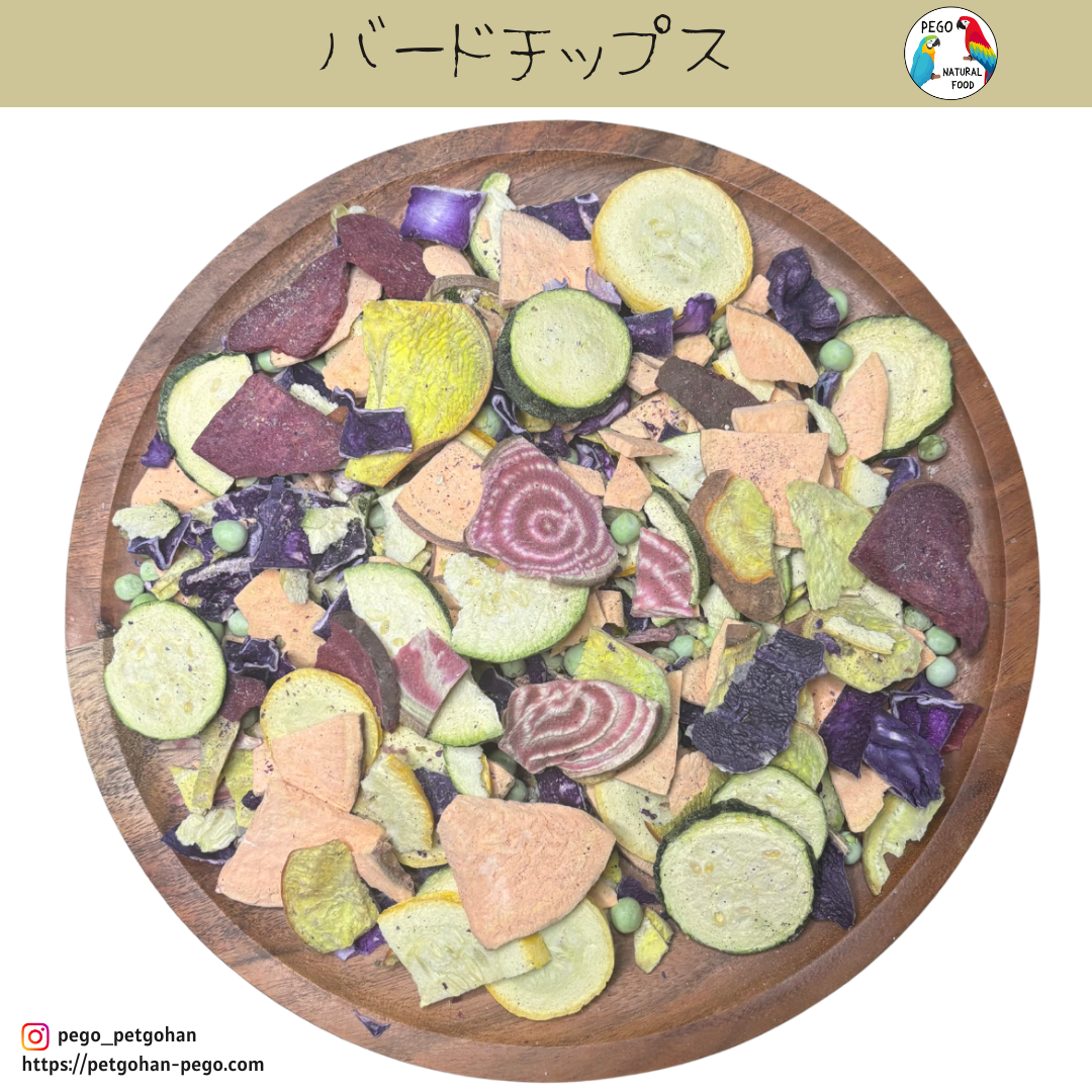 Freeze-dried bird food chips on a wooden plate with beet slices, sweet potato pieces, zucchini rounds, yellow squash, red cabbage, and scattered green peas