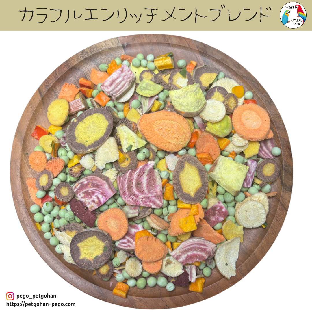 Freeze-dried bird food mix on a wooden plate with green peas, sliced carrots, red and yellow bell pepper pieces, beet slices, and rainbow chard fragments